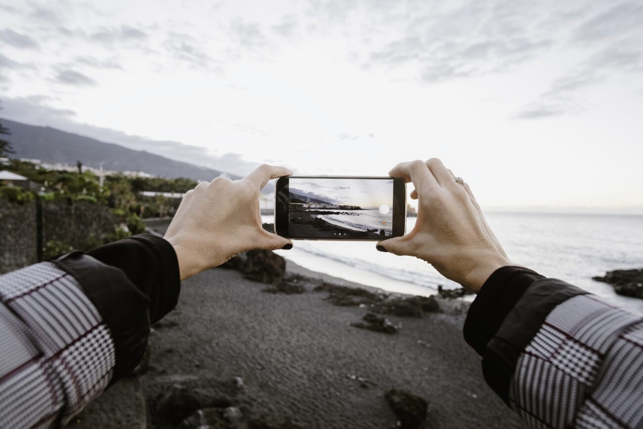 View of a woman taking a picture through his phone of the sea - Pulso Turistico